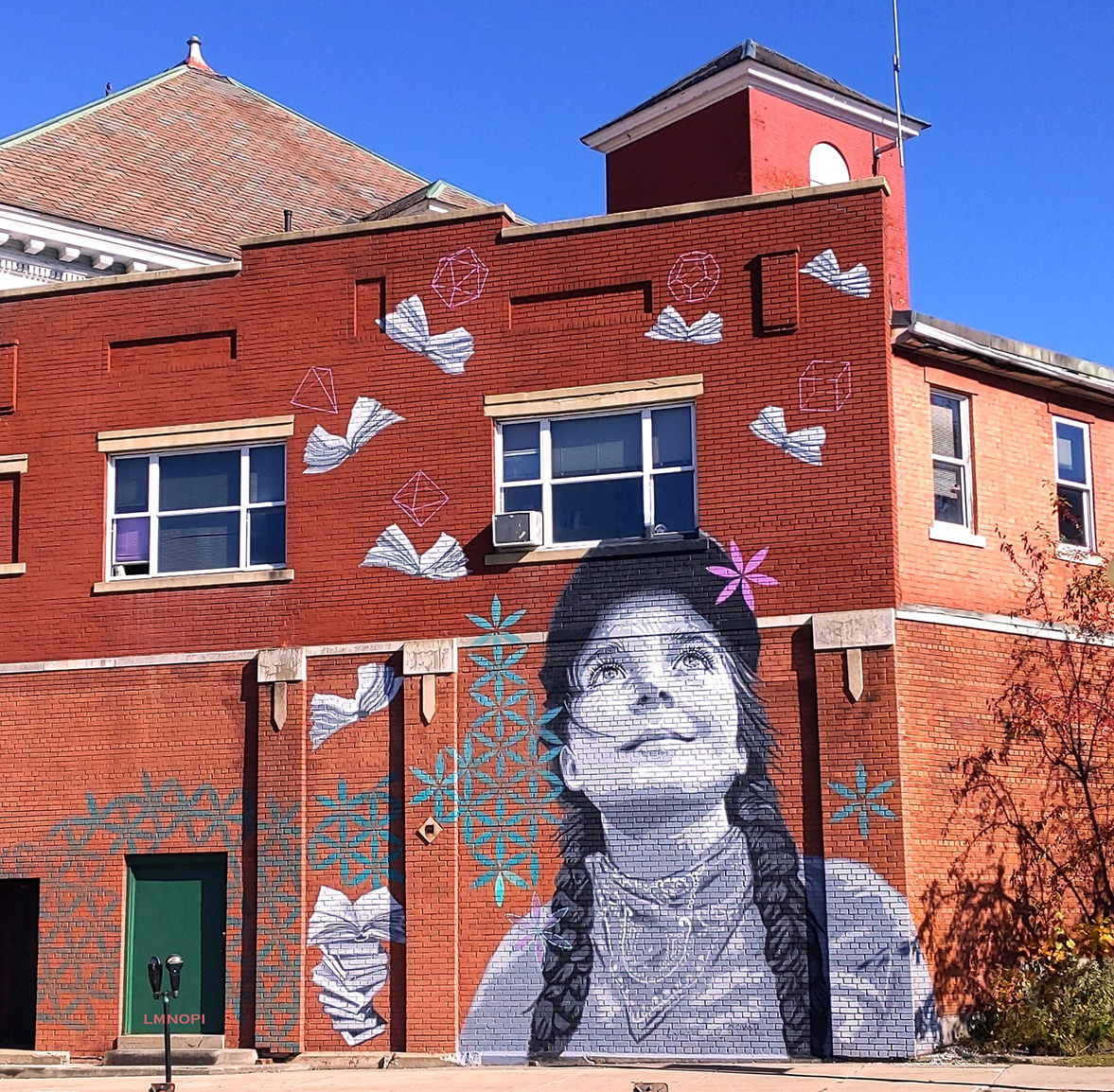 A stunning real-life looking girl looks up from a brick building, but is painted on.