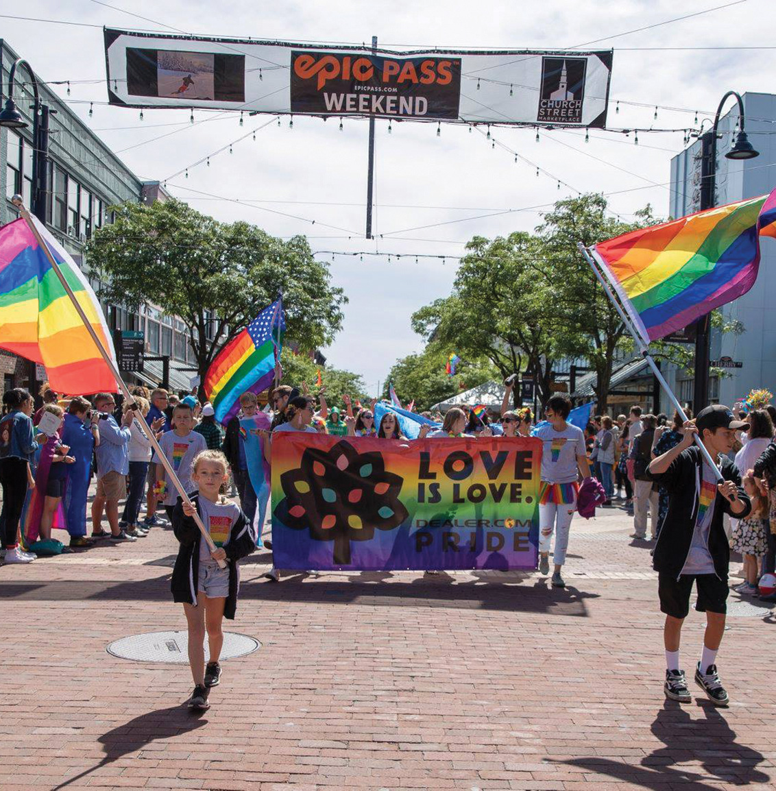 People walk in the pride parade on Church Street in Burlington Vermont surrounded by rainbow flags.