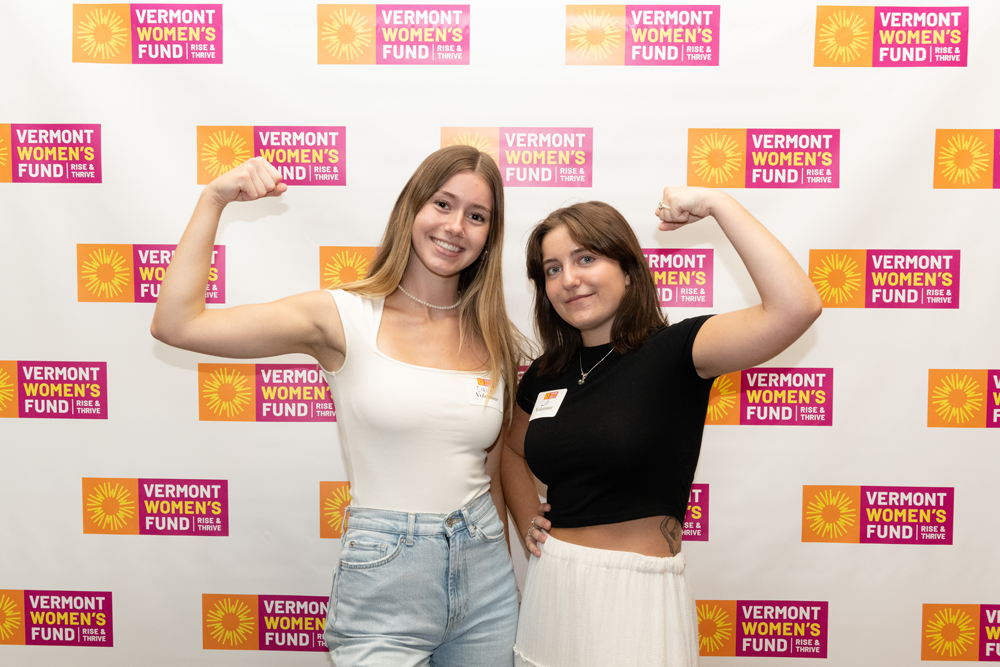 Two girls make muscles in front of a Vermont Women's Fund sign.