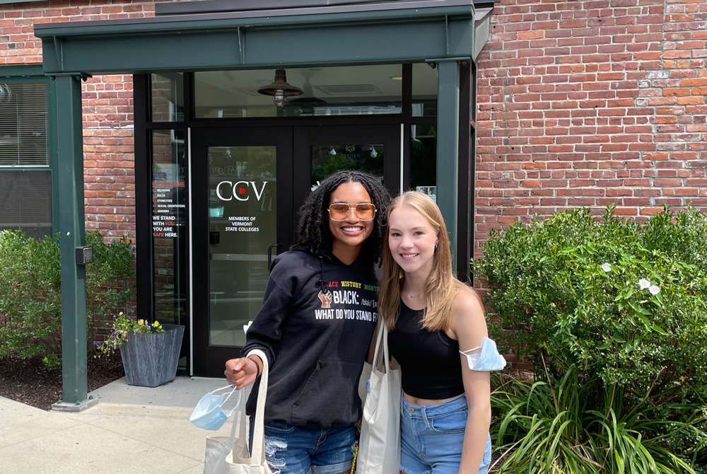 2 young women in jean shorts in front of a brick building with a green overhang in front of a door with the Community College of VT logo on the glass