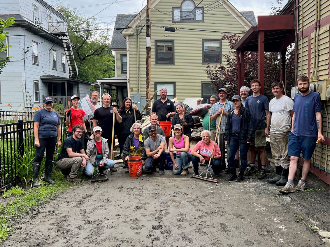 a group of people posing for a photo with shovels and other tools in their hands for cleaning up flood-related mess and mud
