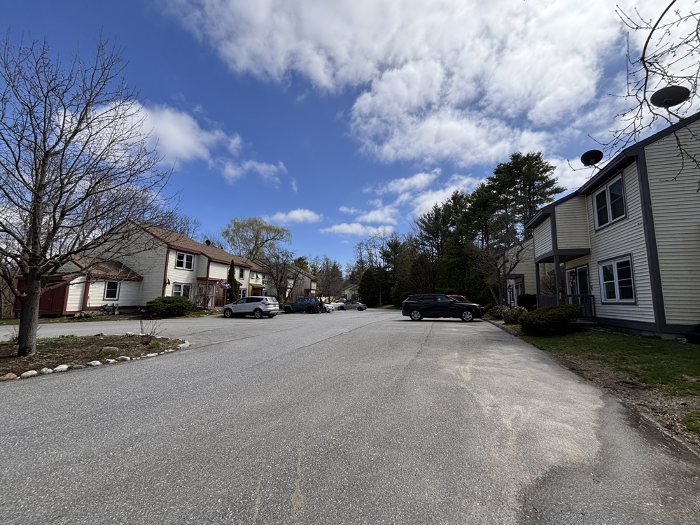 tan apartment buildings with brown trim and cars parked in front of them under a blue sky with light fluffy clouds high above