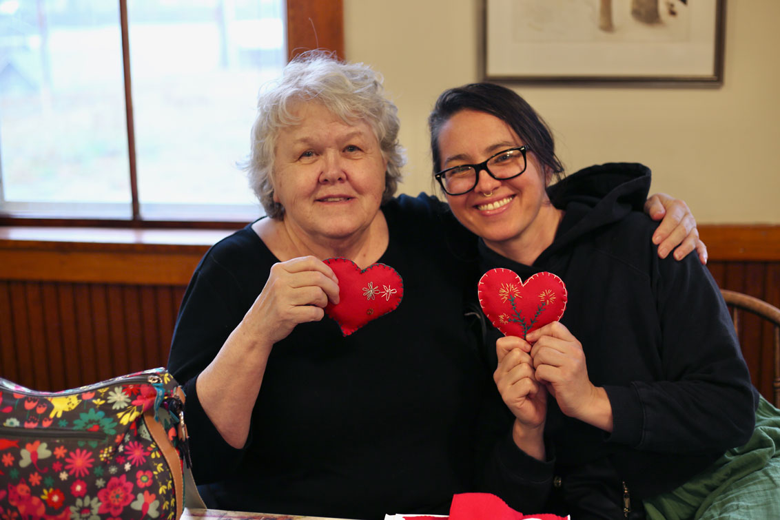 two people hugging and holding up felted hearts they sewed