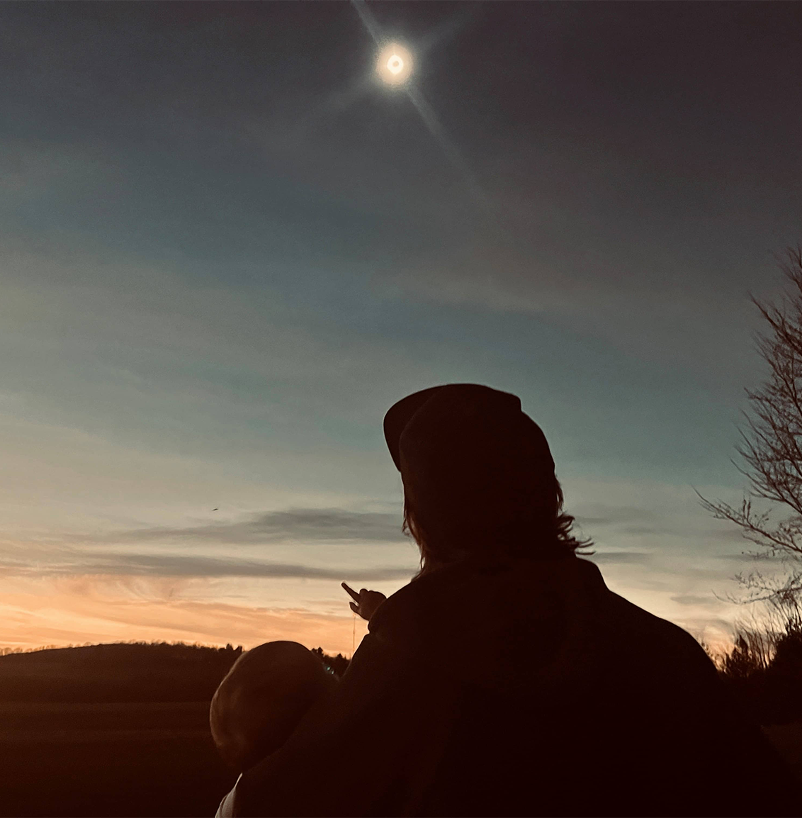 man holding baby looking at eclipse in night sky