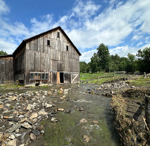 Water rushes in front of a barn during the July floods 2024.