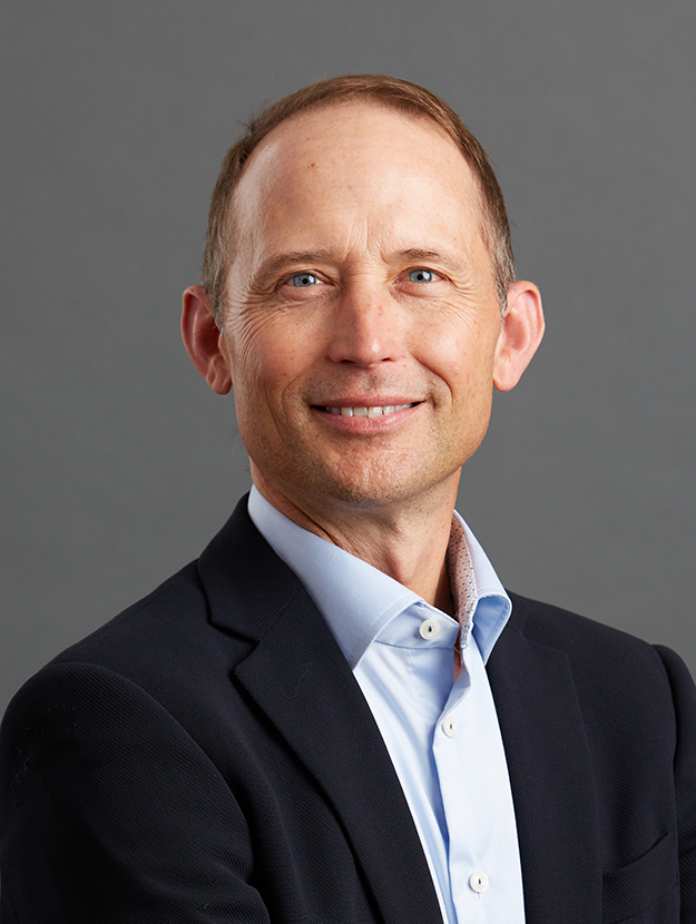 a man with brown hair in a blue button-up shirt and dark blazer