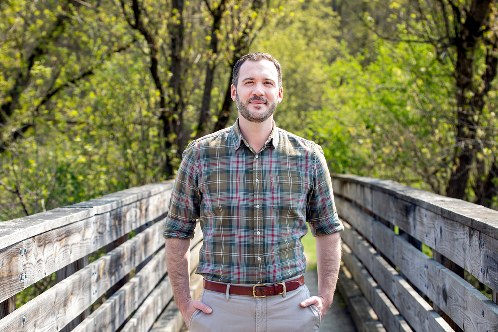 a man in a flannel standing on a wooden footbridge