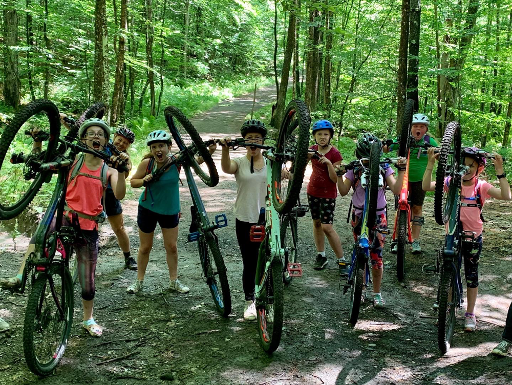 a group of young mountain bikers with their bikes on a wooded path