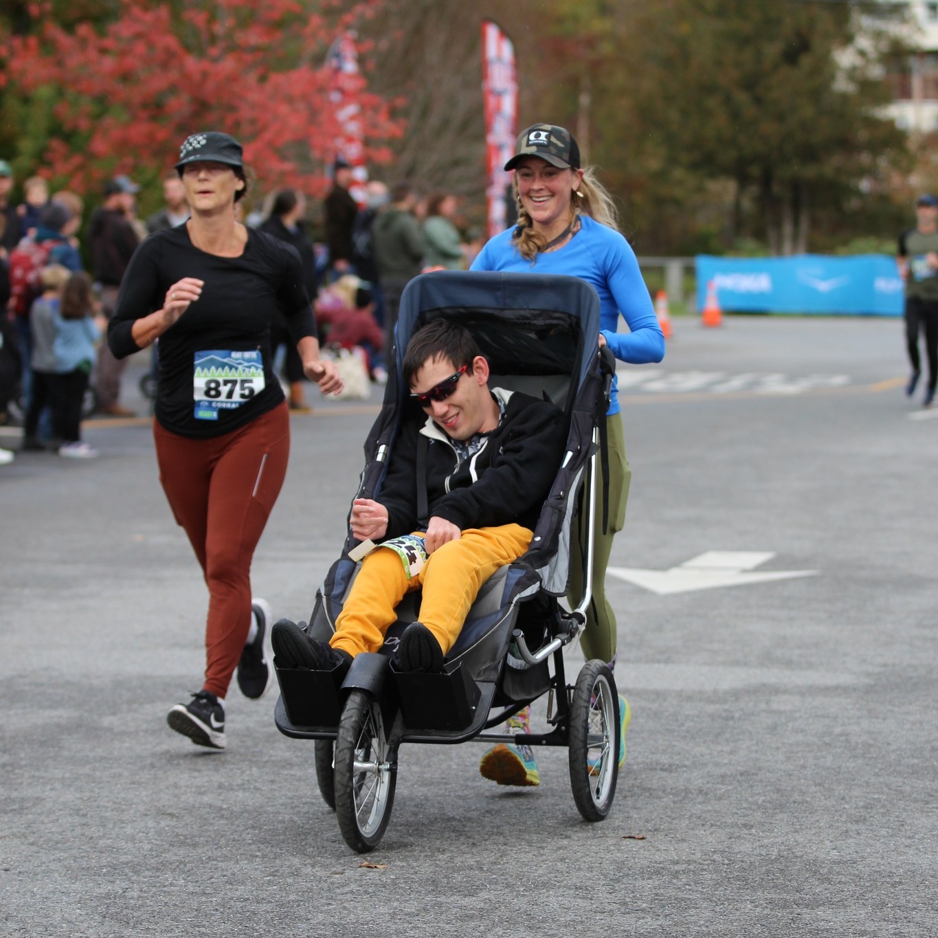 3 individuals running in a race, 2 on foot and 1 in an adaptive wheeled chair