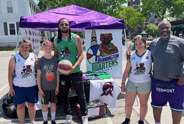 a group people of many ages near a purple pop-up tent, some in basketball uniforms