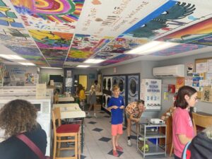 A very decorated laundromat with murals on the ceiling and people walking around.