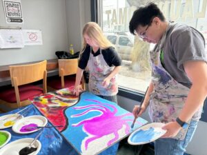 Two people inside painting a large and colorful abstract mural